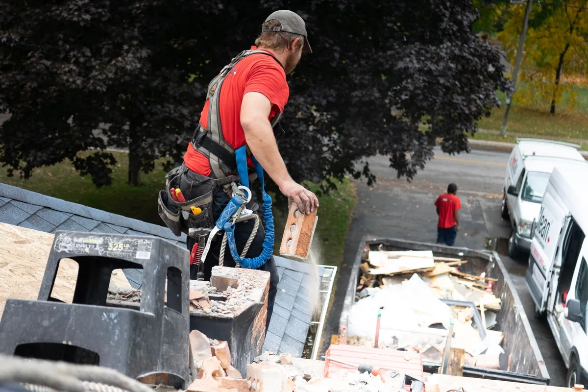 A roofer in a safety harness clearing storm debris