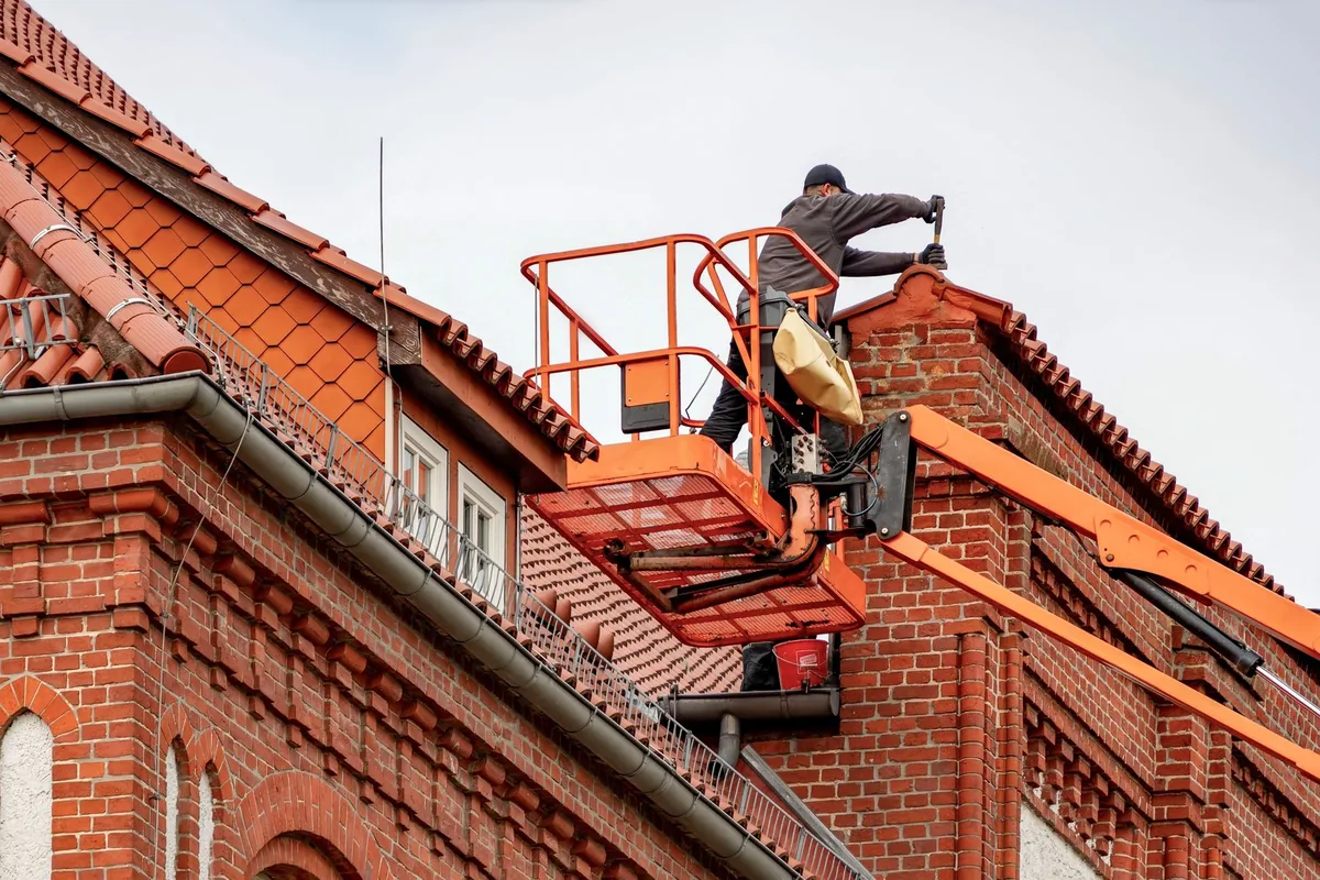 A roofer working from a cherry picker on a brick building